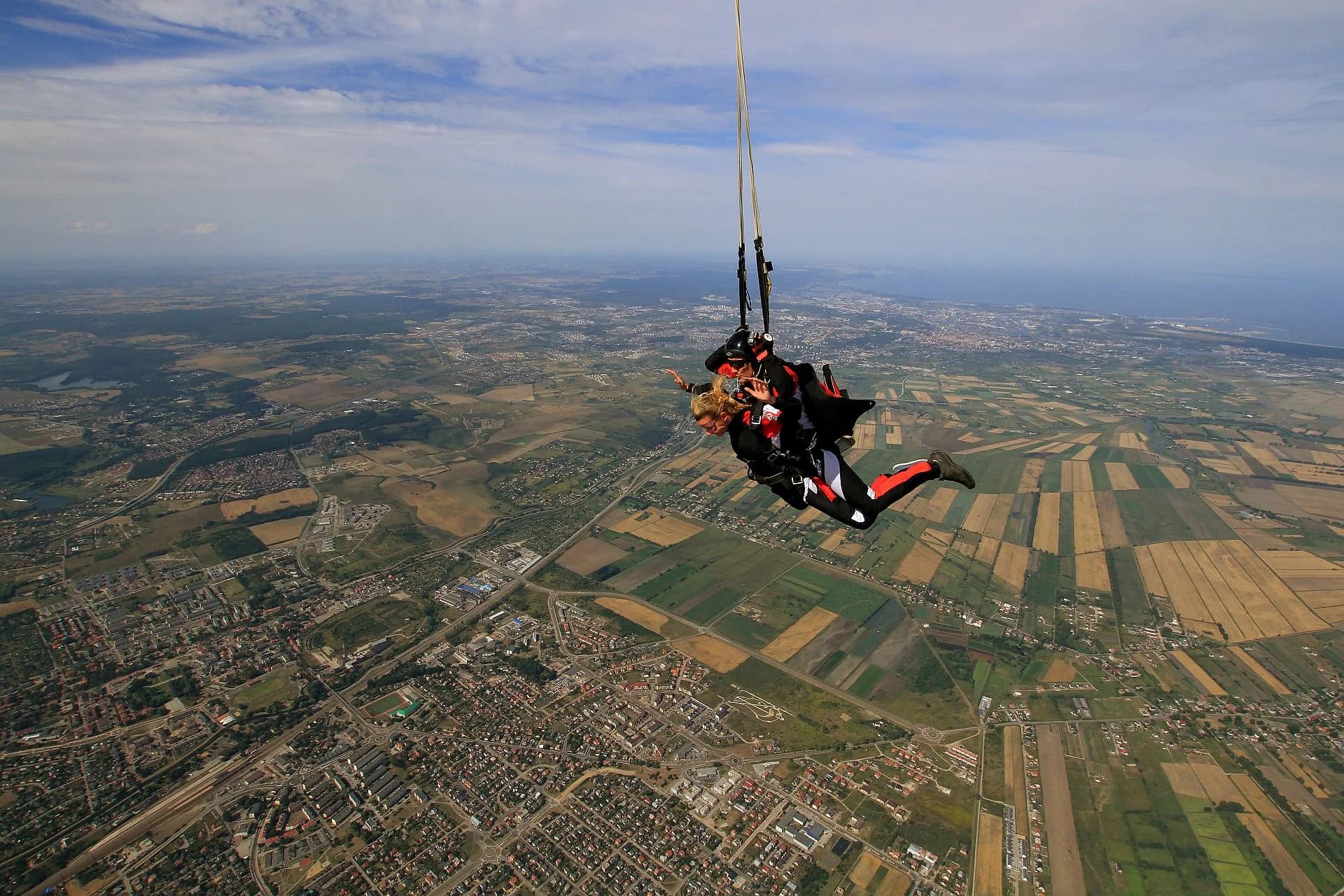 Tandem spada wysoko nad szachownicą pól i miastem — na horyzoncie zatoka